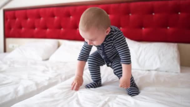 Un niño rubio salta felizmente sobre la cama grande en una habitación de hotel en cámara lenta — Vídeos de Stock