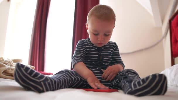 A cute baby clicks smartphone, sitting on the large bed, slow motion — Stock Video