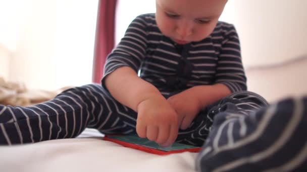 Ребенок увлеченно играет со смартфоном, сидя на кровати, замедленного действия — стоковое видео