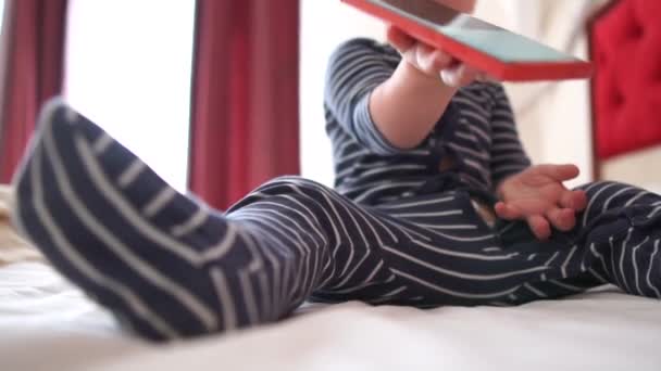 O pequeno bebê alegremente joga o smartphone em uma cama grande em câmera lenta — Vídeo de Stock