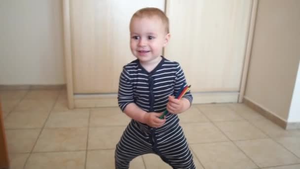 Een kleine jongen houdt potloden en vrolijk dansen in de kamer in slow motion — Stockvideo