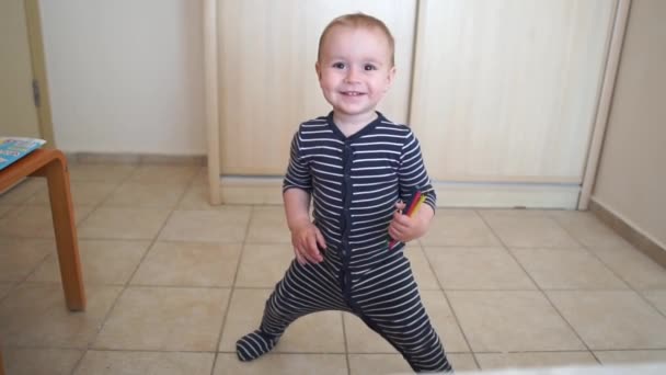 Un chico lindo sostiene lápices y baila alegremente en la habitación en cámara lenta — Vídeo de stock