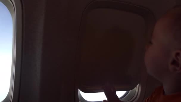 4k - Un niño lindo cierra la cortina del ojo de buey en el avión — Vídeos de Stock