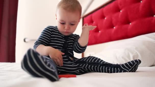 4k - Niño pequeño aplaude alegremente un teléfono inteligente en una cama grande — Vídeos de Stock