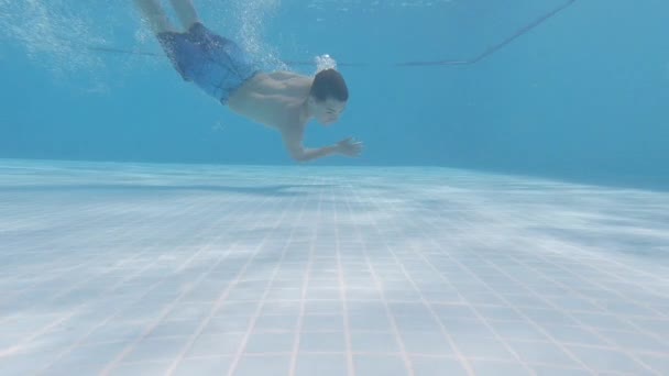 O menino nada debaixo d 'água na piscina e emerge com uma câmera de ação — Vídeo de Stock
