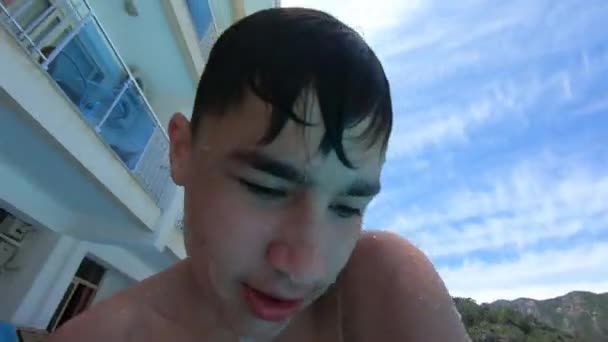 Der Junge steigt mit einer Action-Kamera in Zeitlupe aus dem offenen Hotelpool — Stockvideo