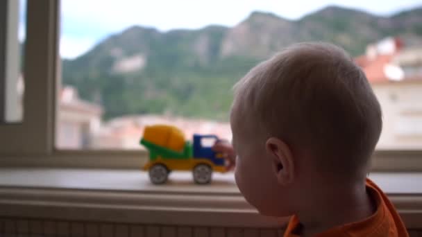 Малыш, стоящий у окна и играющий с грузовиком в замедленной съемке — стоковое видео