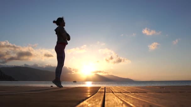 Meisje traint op een houten ponton, springt in slow motion bij zonsondergang — Stockvideo