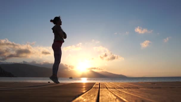 Chica entrena en un pontón de madera, salta en cámara lenta al atardecer — Vídeos de Stock