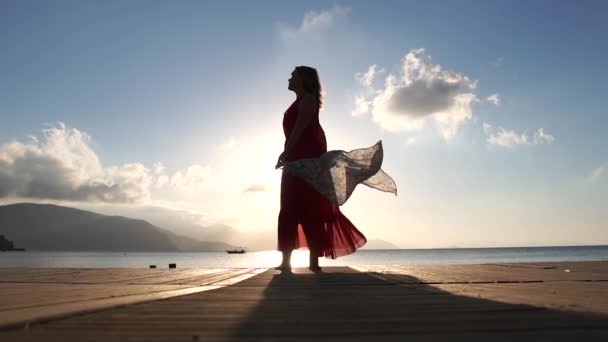 Una mujer adulta con una bufanda se para en la playa al amanecer en cámara lenta — Vídeos de Stock