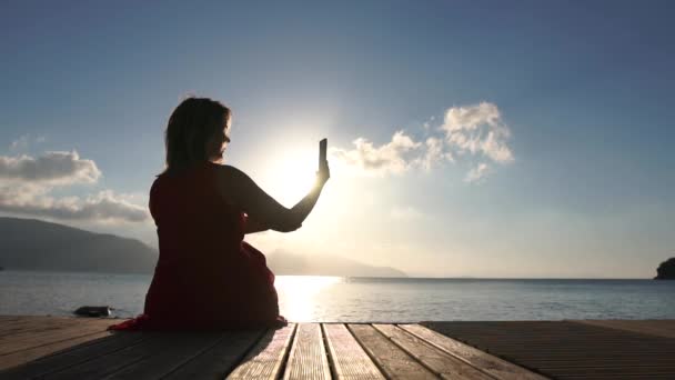 Una mujer toma fotos en el teléfono inteligente, sentado en el pontón en cámara lenta — Vídeos de Stock