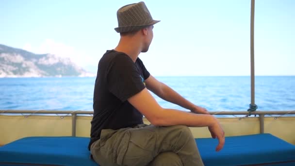 Young brunette guy in a hat is floating on a boat in slow motion — Stock Video