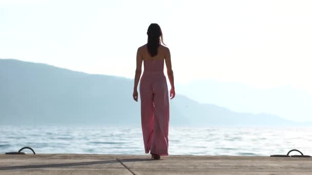 Mulher caminha em frente ao mar e posa como um modelo no pódio em câmera lenta — Vídeo de Stock