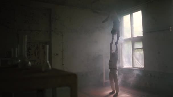 Satu pria tangguh berdiri dan yang kedua melakukan membungkuk berdiri kembali handstand di ruang di slo-mo — Stok Video