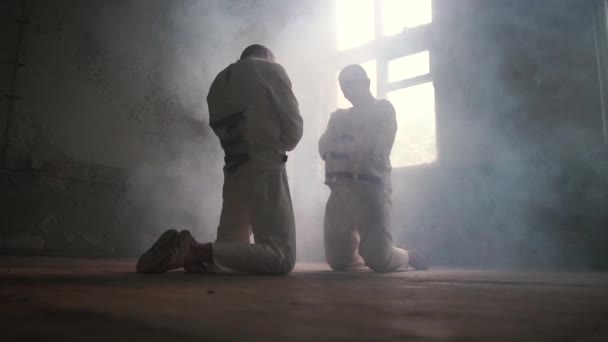 Двоє божевільних чоловіків на колінах один проти одного, дивлячись в сторону в психіатричній лікарні в шлю-мо — стокове відео