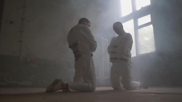 Two wack men kneeling against each other, looking aside in mental house in slo-mo — Stock Video
