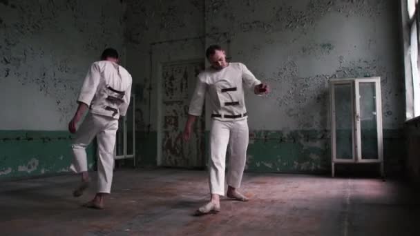 흰색 유니폼을 입은 두 명의 사이코 남성이 초라한 홀에서 점프하고 춤을 추고 있습니다. — 비디오