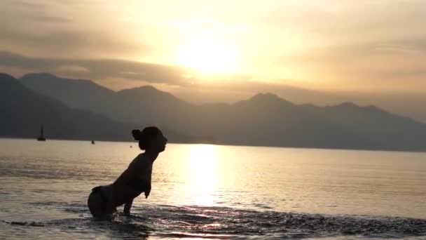 Красивая девушка красиво брызгает водой в море в замедленной съемке на рассвете — стоковое видео