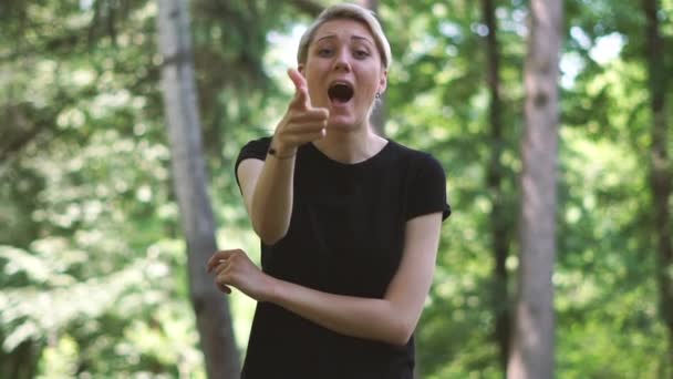 Lycklig blond kvinna stående och visar två finger pistol gester utomhus i slo-mo — Stockvideo