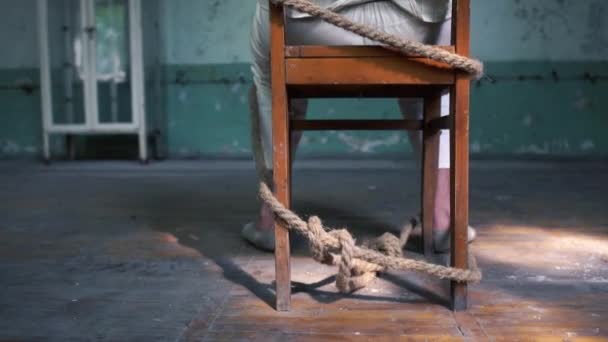 Un loco sentado atado a una vieja silla azul en una habitación de mala muerte — Vídeo de stock