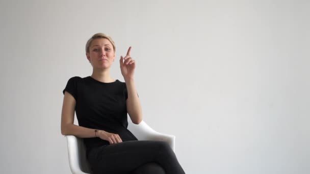 Mulher loira jovem elegante sentado e aumentando seu índice em um estúdio branco em slo-mo — Vídeo de Stock