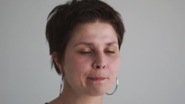 Divertente ragazza bruna con piercing al naso seduta e pensare duramente in uno studio in slo-mo — Video Stock