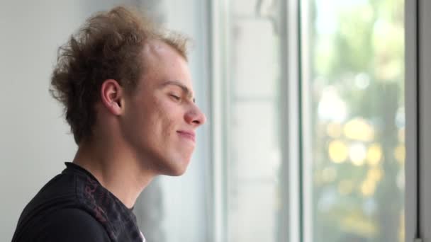Hombre divertido mirando por la ventana y mirando a un lado con una sonrisa en un estudio en slo-mo — Vídeos de Stock