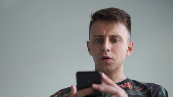 Joven mirando su teléfono inteligente con una sonrisa impactante en el estudio en slo-mo — Vídeos de Stock