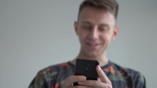 Cara surpreso olhando para seu smartphone com um sorriso impressionante no estúdio em slo-mo — Vídeo de Stock