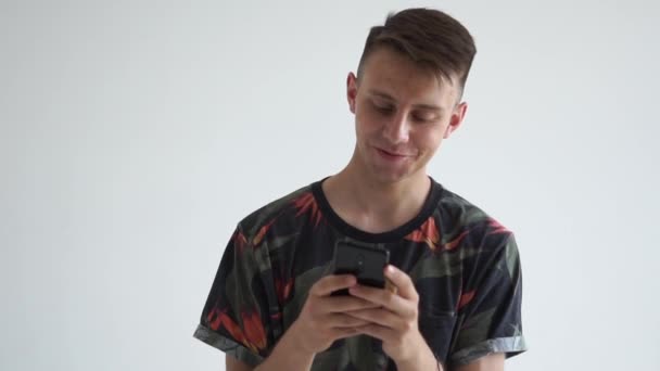 Chico feliz mirando a su smartphone con una sonrisa romántica en el estudio en slo-mo — Vídeos de Stock