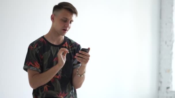 Inspirierter Kerl, der auf sein Smartphone schaut und glücklich im Studio in Slo-mo eine SMS schreibt — Stockvideo