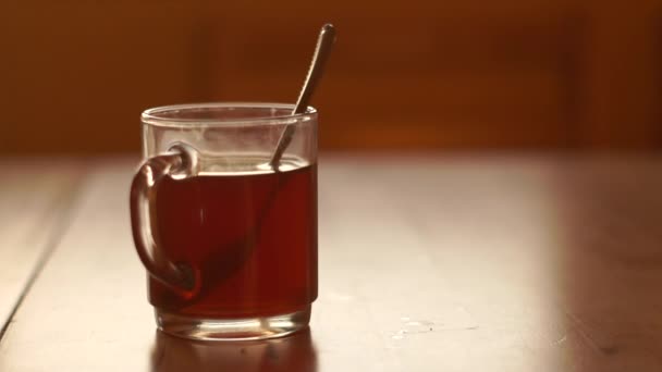 Egy átlátszó csésze tea áll egy asztalon egy vaskanál belül a reggeli nap. — Stock videók