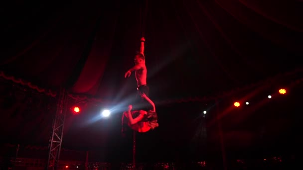 Мужчина-гимнаст берет девочку с ногами, пока она гадит в цирке по ночам в сло-мо — стоковое видео