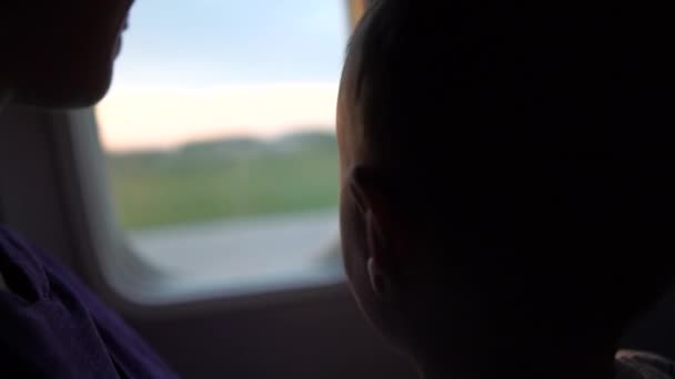 Mamá con un niño se sienta en la ventana de un avión durante el amanecer del sol - 4k . — Vídeos de Stock