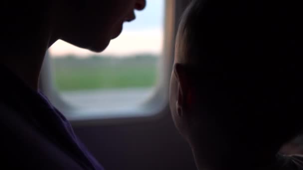 Máma s dítětem sedí u okna letadla během úsvitu slunce-4k. — Stock video