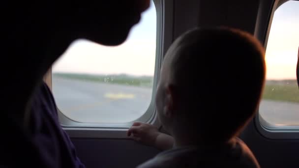 Moeder met een kind zit aan het raam van het vliegtuig terwijl het vliegtuig begint af te nemen — Stockvideo