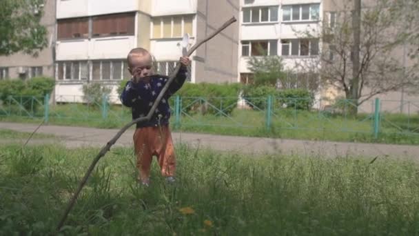 Vrolijke blonde Kid houdt en gooit een tak in een gazon in de zomer in slo-mo — Stockvideo