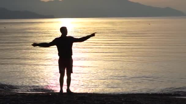 Yavaş çekimde gün doğumunda deniz kıyısında dans eden genç adam — Stok video