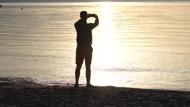 一个英俊的男人在智能手机上慢动作拍摄早晨的海景 — 图库视频影像