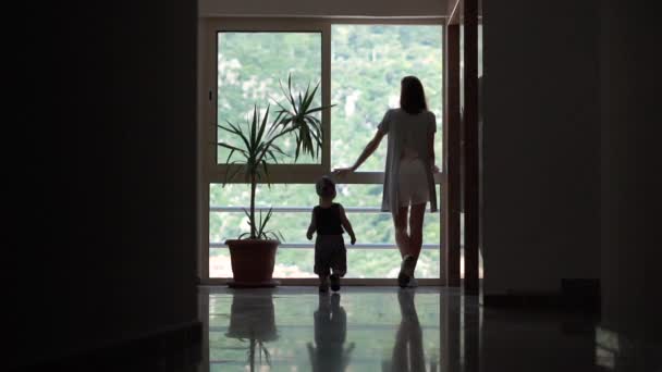 Маленький мальчик идет к большому окну к своей маме, вид сзади, замедленная съемка — стоковое видео
