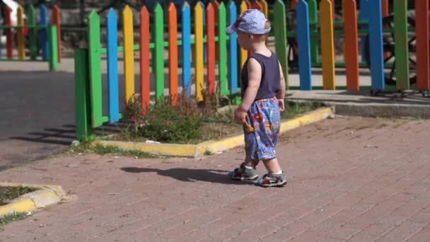 Un niño pequeño va al patio de recreo más allá de una hermosa cerca en cámara lenta — Vídeos de Stock