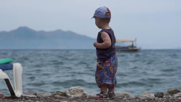 Un niño pequeño y lindo lanza piedras al mar en cámara lenta — Vídeos de Stock