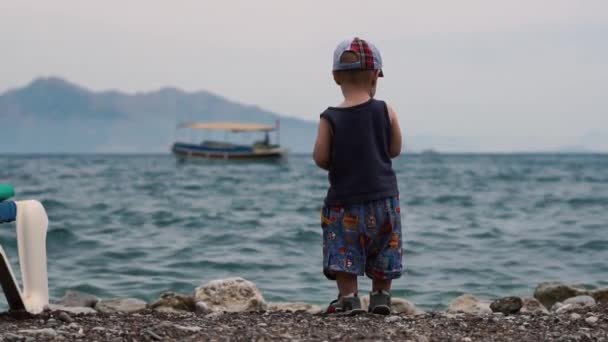 En liten pojke kastar stenar till sjöss i slow motion — Stockvideo