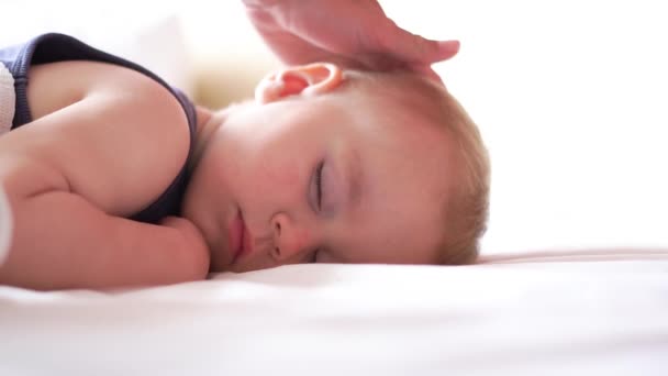 Mamá acaricia la cabeza de los bebés mientras él duerme dulcemente en una cama grande en cámara lenta — Vídeos de Stock