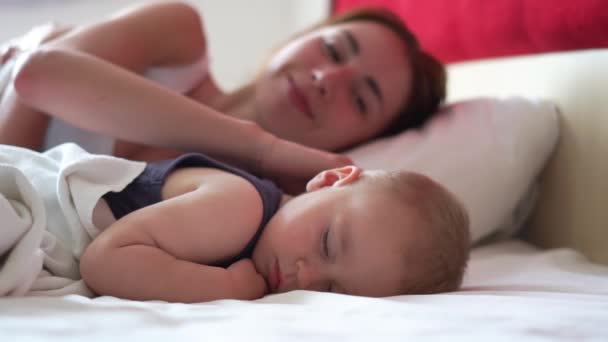 Elég fiatal anya megcsókolja a gyereket az arcán, miközben ő édesen alszik — Stock videók