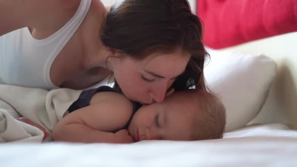 Jovem mulher beija o bebê na bochecha enquanto ele dorme docemente em câmera lenta — Vídeo de Stock
