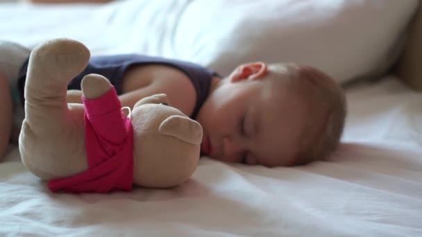 Schattige baby slaapt op het grote bed met zijn geliefde teddybeer in slow motion — Stockvideo
