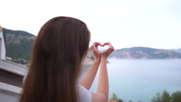 Una ragazza ha fatto una forma di cuore dalle sue mani su uno sfondo di mare, al rallentatore — Video Stock