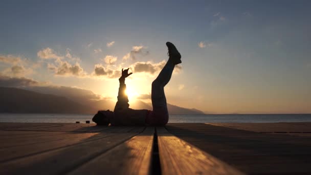 4k - La ragazza allena gambe e braccia sdraiata vicino al mare al rallentatore al tramonto — Video Stock