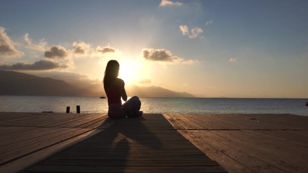 4k - Hermosa chica atlética reza al amanecer junto al mar en cámara lenta — Vídeos de Stock